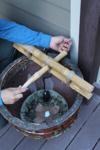 man threading plastic tubing in to bamboo spout and down in to the large pot